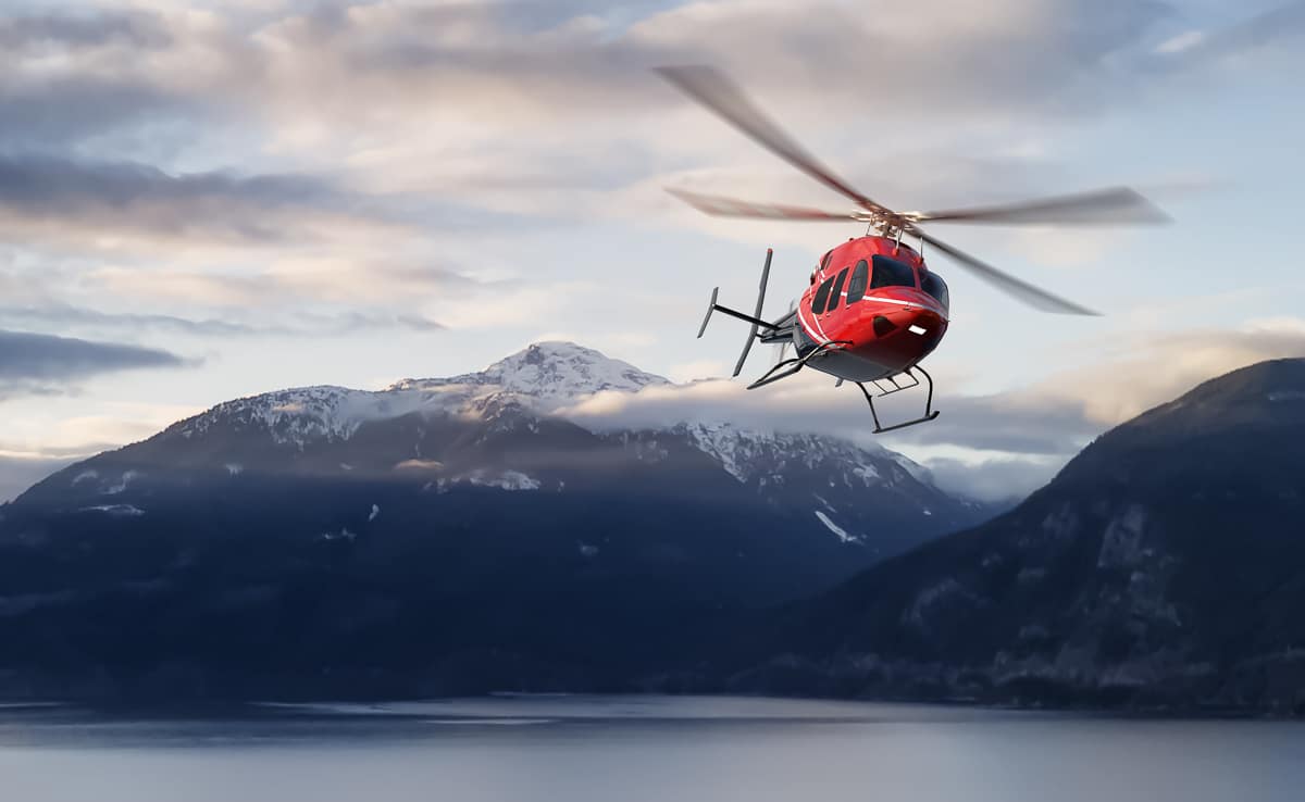 Helikopter i lav høyde over fjordlandskap med fjell i bakgrunnen.